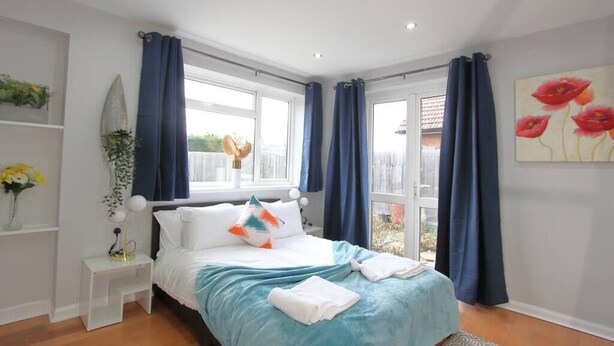A bedroom with a bed, a nightstand, a window with curtains, and a painting on the wall.