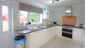 A modern kitchen with white cabinets, a stainless steel sink, a microwave, a stove, and a window with a view of greenery.