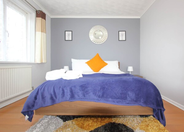 Une chambre à coucher comprenant un lit, deux lampes de chevet, une fenêtre avec des rideaux, un radiateur et un miroir fixé au mur.
