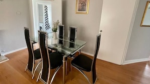 A dining area with a glass table and black chairs, a white door, and a framed picture on the wall.