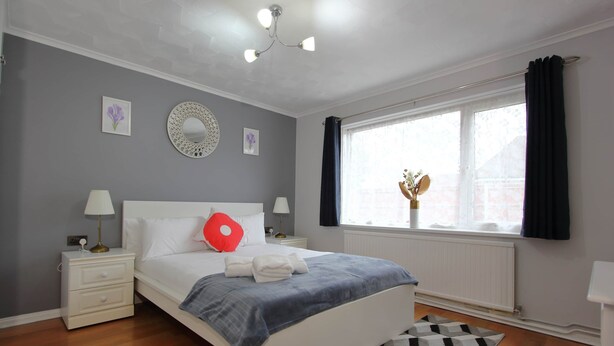 A modern bedroom with a bed, nightstands, a window with curtains, and a decorative mirror.
