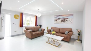 A modern living room with two sofas, a coffee table, a chandelier, a painting, and a clock on the wall. - Elegant 4 Bed 3 Bath House & Parking by CozyNest (Reading)