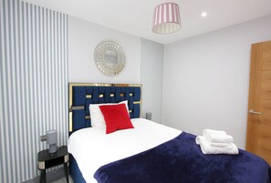 Une chambre d’hôtel avec un lit, une table de chevet, une lampe, un miroir et une porte.