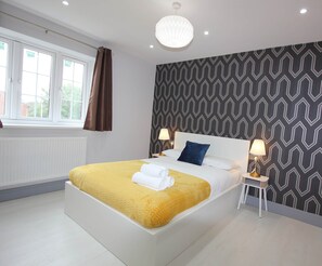 Et moderne hotelværelse med en stor seng, to sengeborde med lamper, en tapetvæg og et vindue med gardiner.