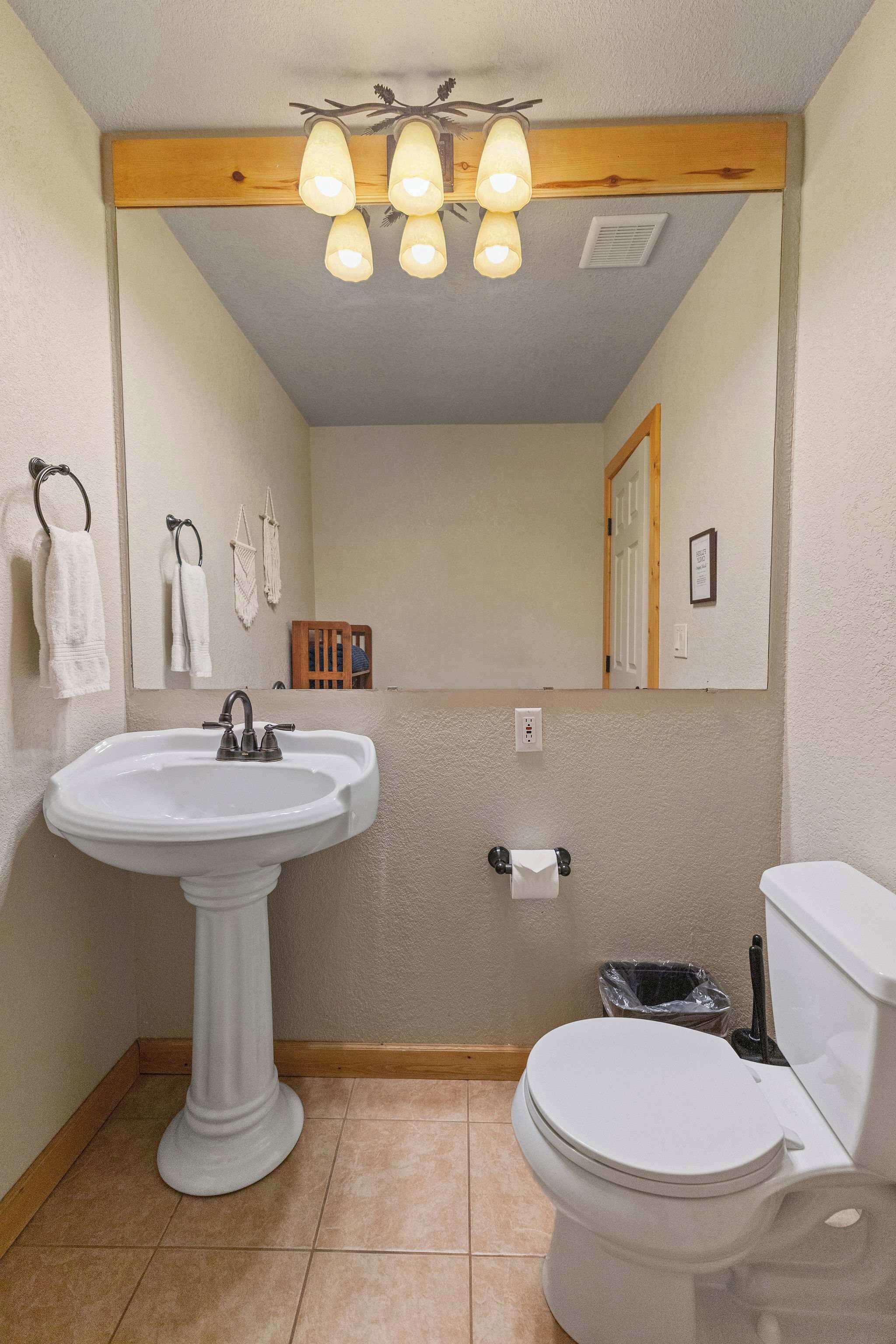 Een badkamer met een wastafel op een voetstuk, een toilet en een spiegel.