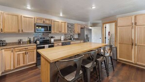 A modern kitchen with wooden cabinets, a granite countertop, stainless steel appliances, and a central island with bar stools.