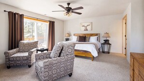 A bedroom with a bed, two chairs, a ceiling fan, a lamp, and a deer painting on the wall.