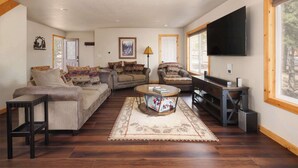A living room with a sofa, armchair, coffee table, and a flat-screen TV.