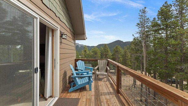 A wooden deck with two Adirondack chairs, a glass door entrance, and a view of trees and mountains.
