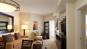 Quarto de hotel moderno com área de refeições, sala de estar e cozinha compacta.