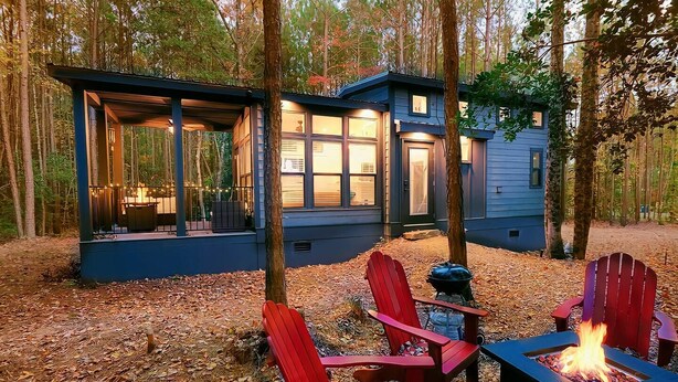 Eine Hütte mit einer Veranda, einem Feuerkorb und roten Adirondack-Stühlen.