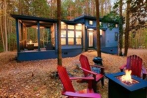 Mökki, jossa on terassi, nuotiopaikka ja punaiset Adirondack-tyyliset puutarhatuolit.