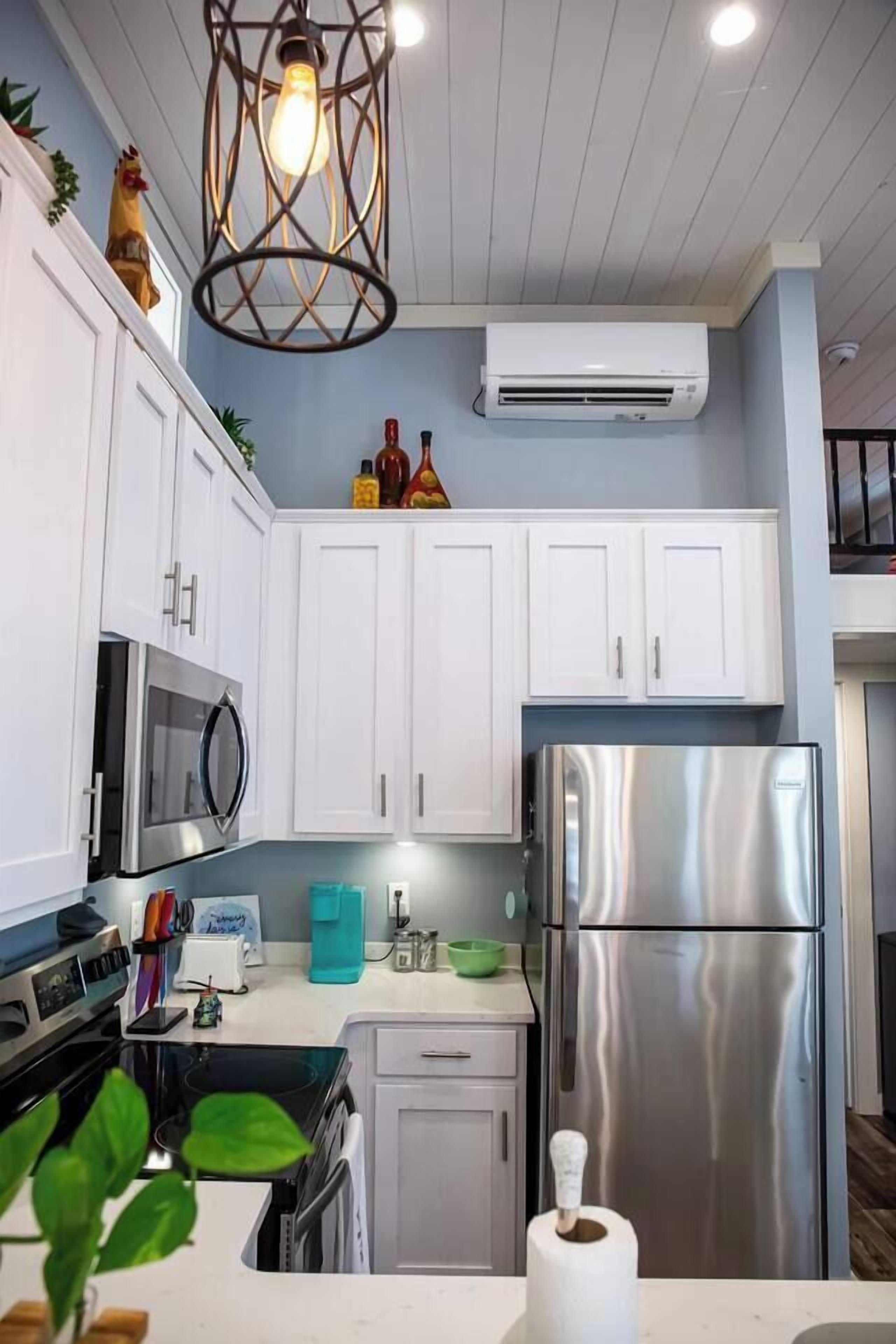 A modern kitchen with white cabinets, stainless steel appliances, and a unique pendant light fixture.