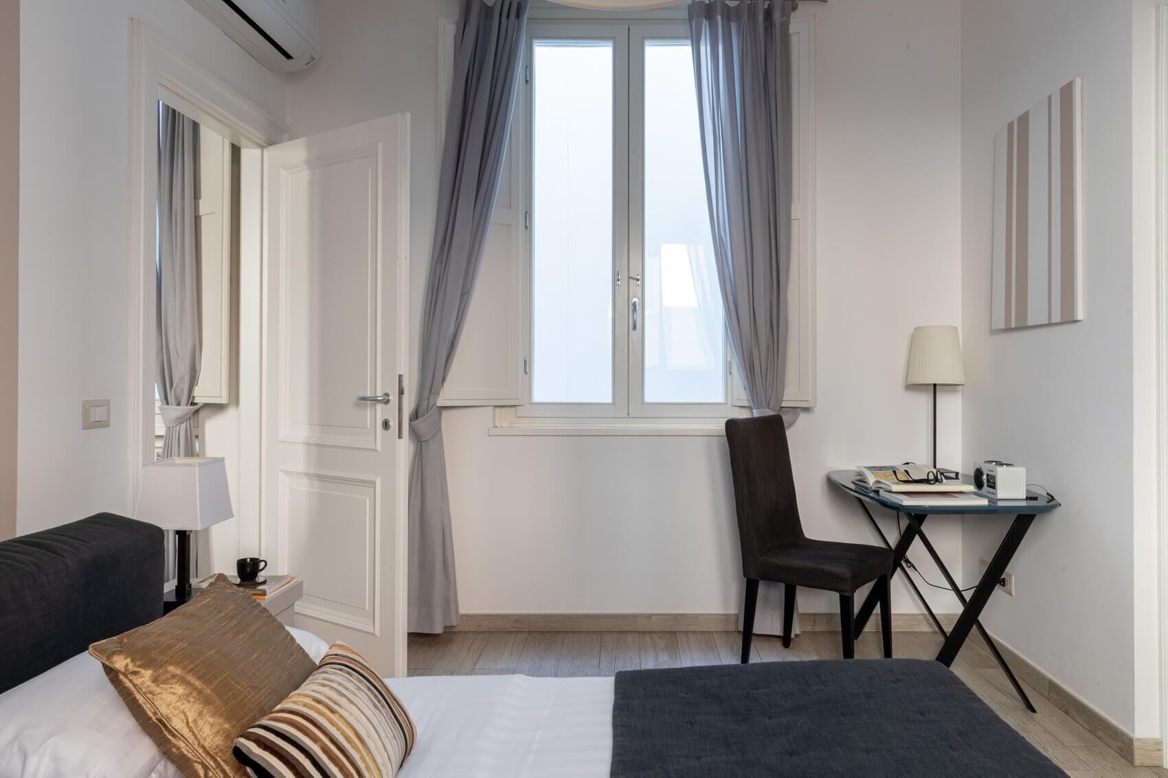 Ein Hotelzimmer mit einem Bett, einem Schreibtisch mit Stuhl, einer Lampe und einem Fenster mit Vorhängen.
