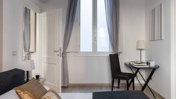 Ein Hotelzimmer mit einem Bett, einem Schreibtisch mit Stuhl, einer Lampe und einem Fenster mit Vorhängen.