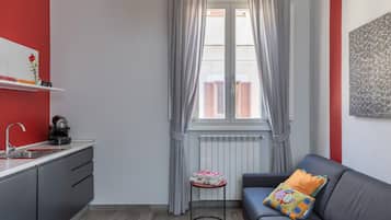 Un espacio habitable compacto con kitchenette, un sofá y un ventanal con cortinas.