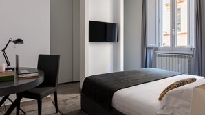 Una habitación de hotel moderna con una cama, un escritorio con una computadora portátil, una silla, un televisor montado en la pared y una ventana con cortinas.