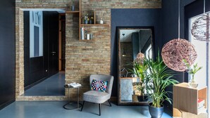 Un interior moderno con pared de ladrillo, un espejo grande, una silla con un cojín colorido y plantas en macetas.