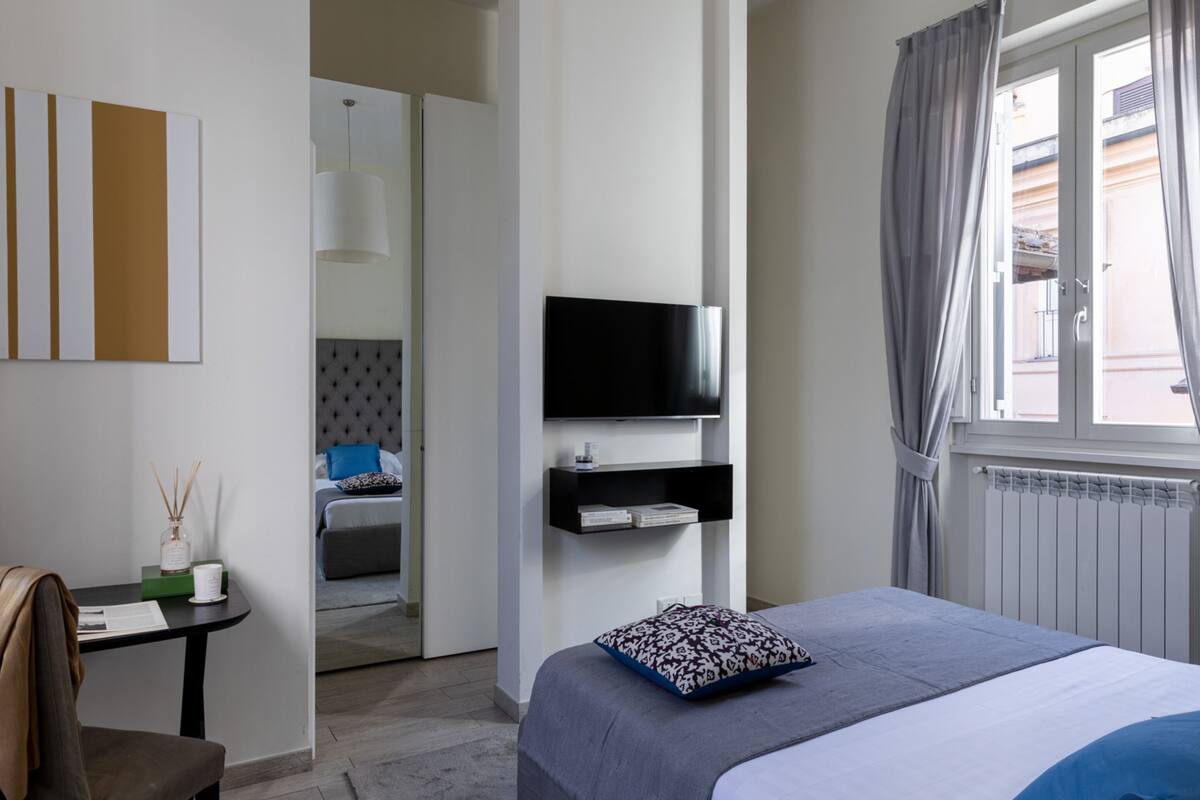 Une chambre d’hôtel moderne, équipée d’un lit, d’un téléviseur fixé au mur, d’une petite table avec une bougie, et offrant une vue sur l’extérieur par une fenêtre.
