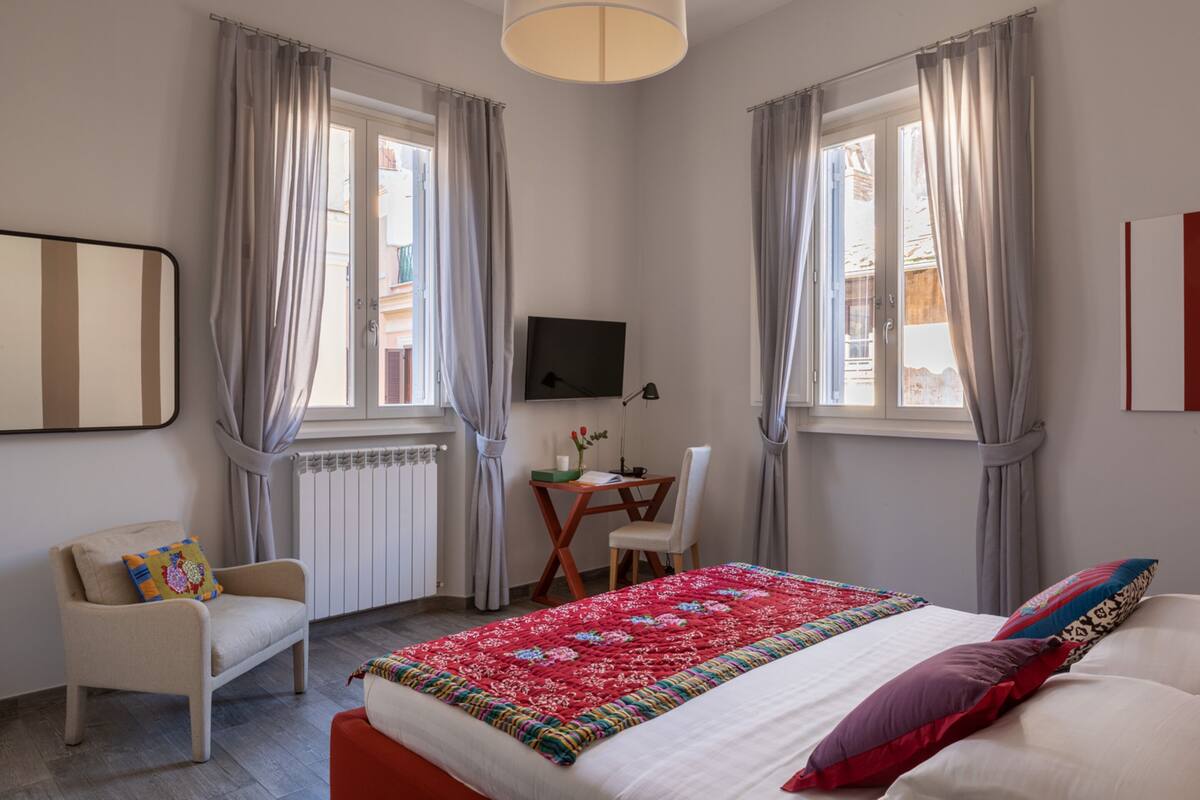 Une chambre d’hôtel avec un lit, un bureau et une chaise, une télévision et une fenêtre avec des rideaux.
