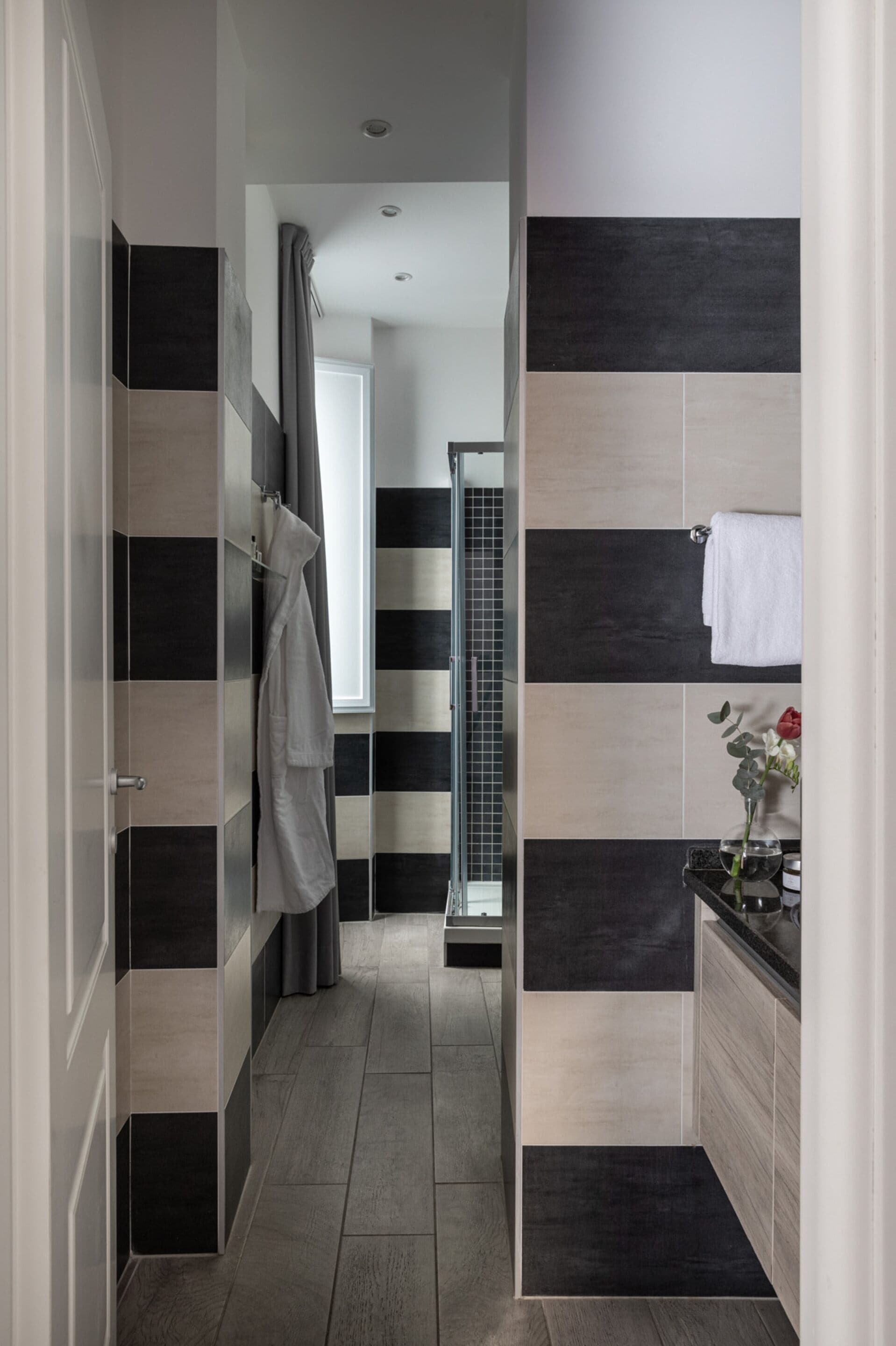 Ein modernes Badezimmer mit schwarz-weißen Streifenfliesen, einer Glasdusche und einem Waschbecken mit Blumen in einer Vase.