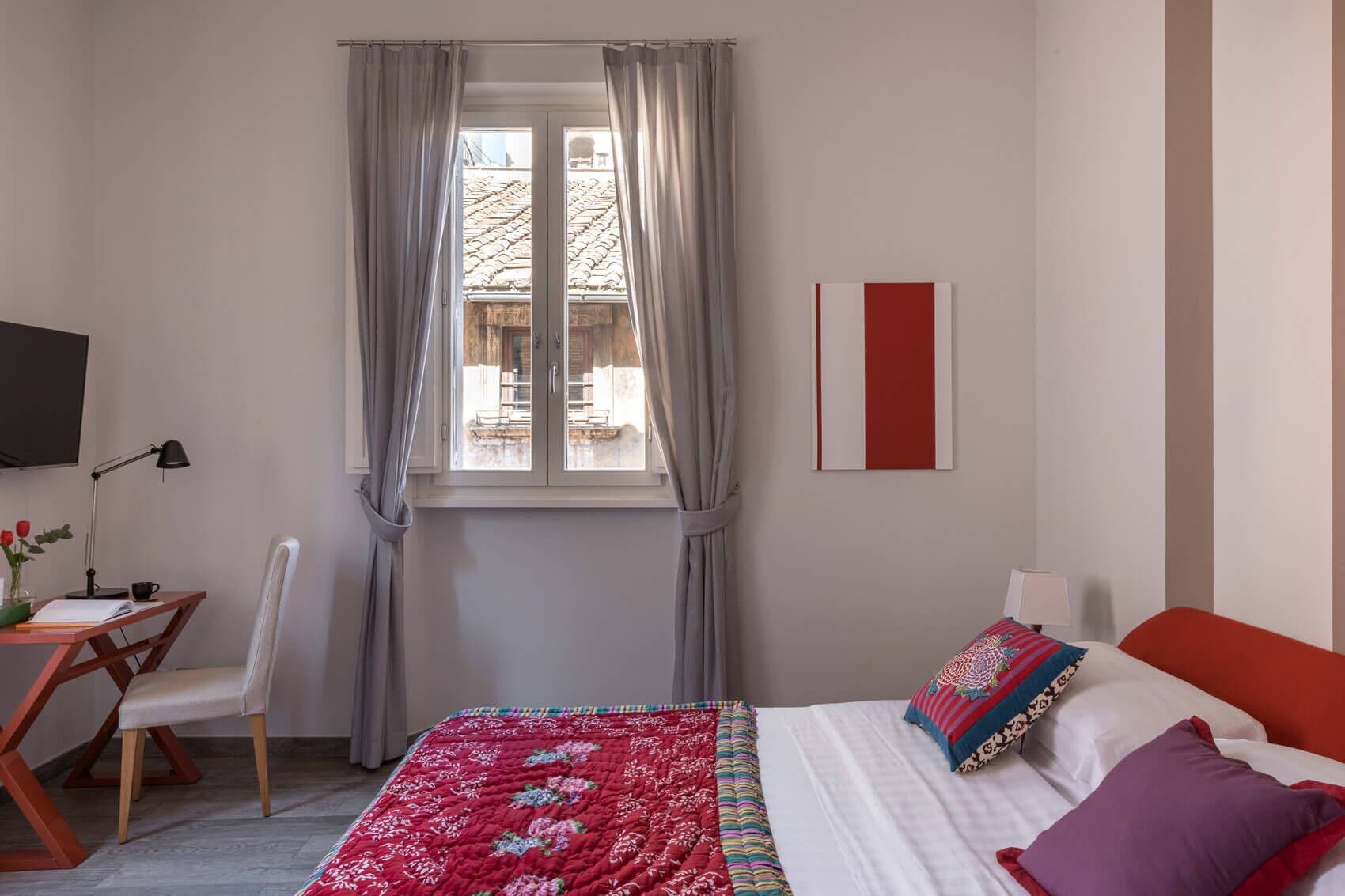 Ein Schlafzimmer mit einem Bett, einem Schreibtisch, einem Stuhl, einem Fernseher und einem Fenster mit Vorhängen.