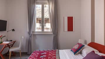 Un dormitorio con cama, escritorio, silla, televisión y ventana con cortinas.
