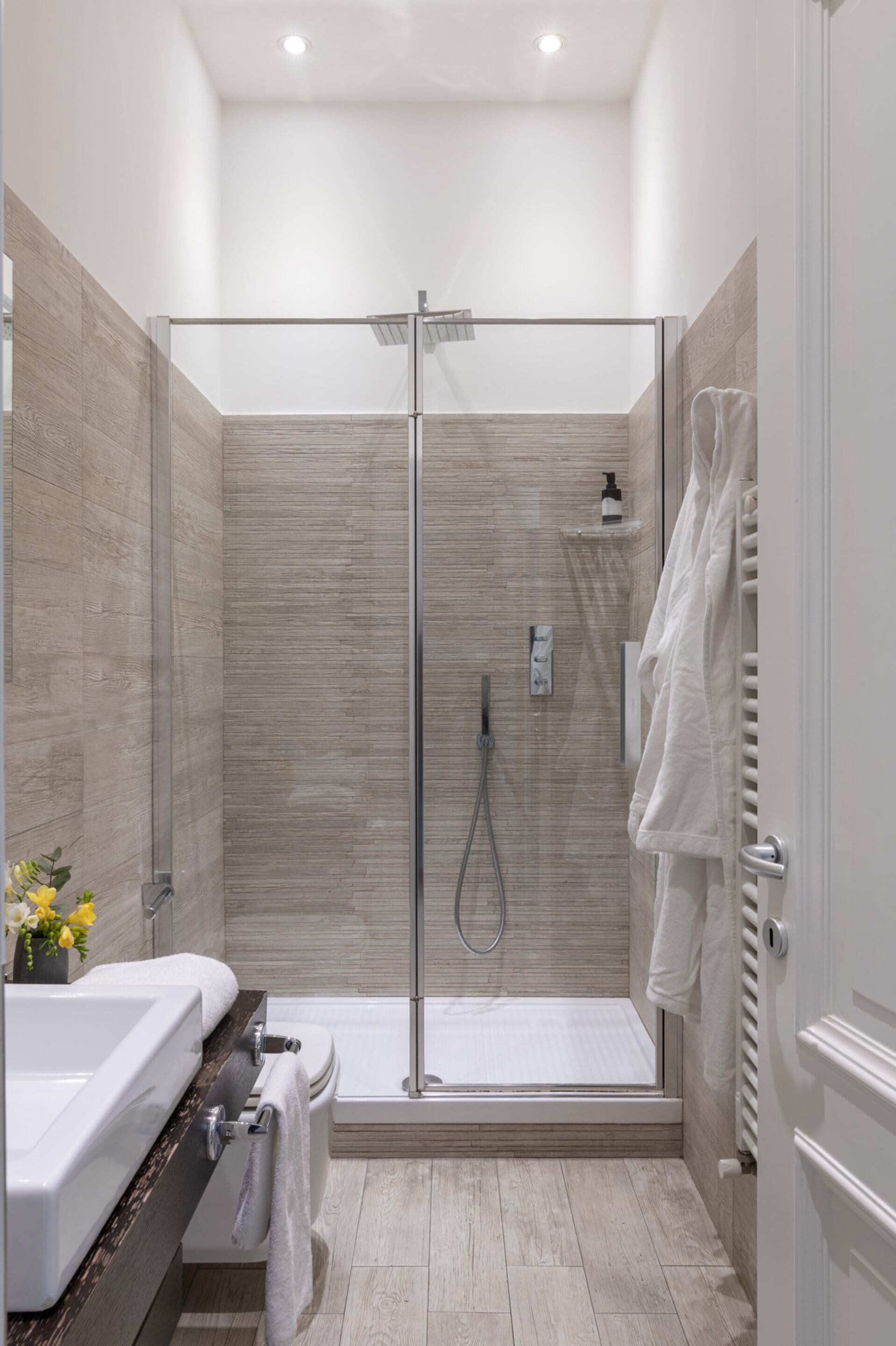 A modern bathroom with a glass-enclosed shower, a bathtub, and a vanity with a towel rack.