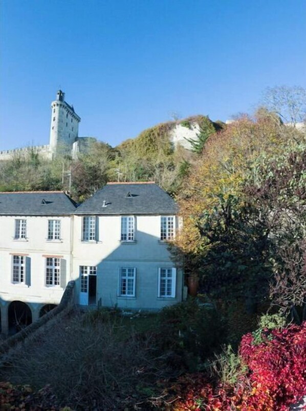 A two-story building with a tower, surrounded by dense foliage and autumn-colored trees.