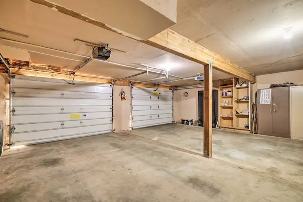 Un garage con due porte basculanti bianche, una struttura a travi di legno e un pavimento in cemento.