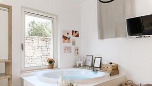 Une salle de bain moderne avec une grande baignoire, un mur en pierre et des œuvres d’art accrochées au mur.