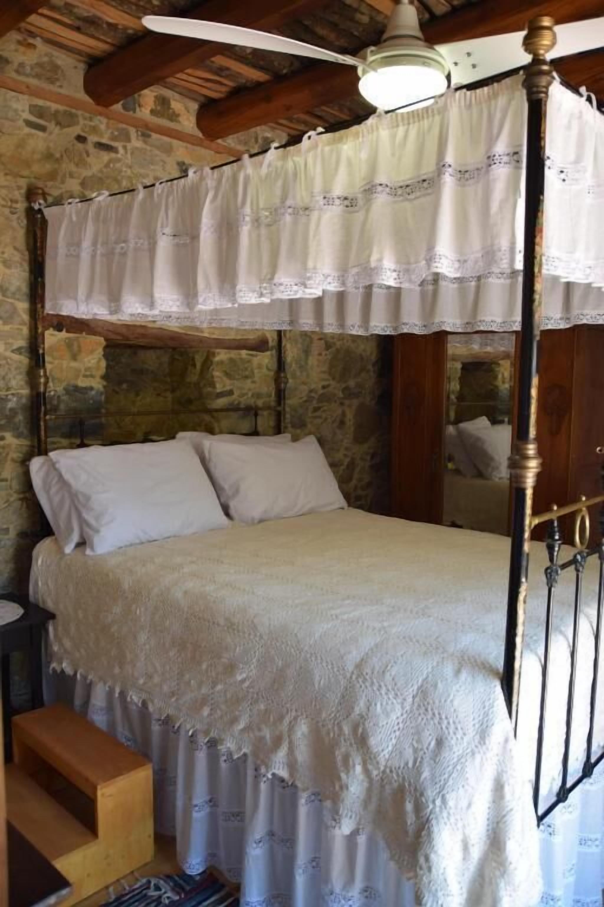 Un lit à baldaquin avec des poteaux aux quatre coins, un mur en pierre en arrière-plan et un escalier en bois.
