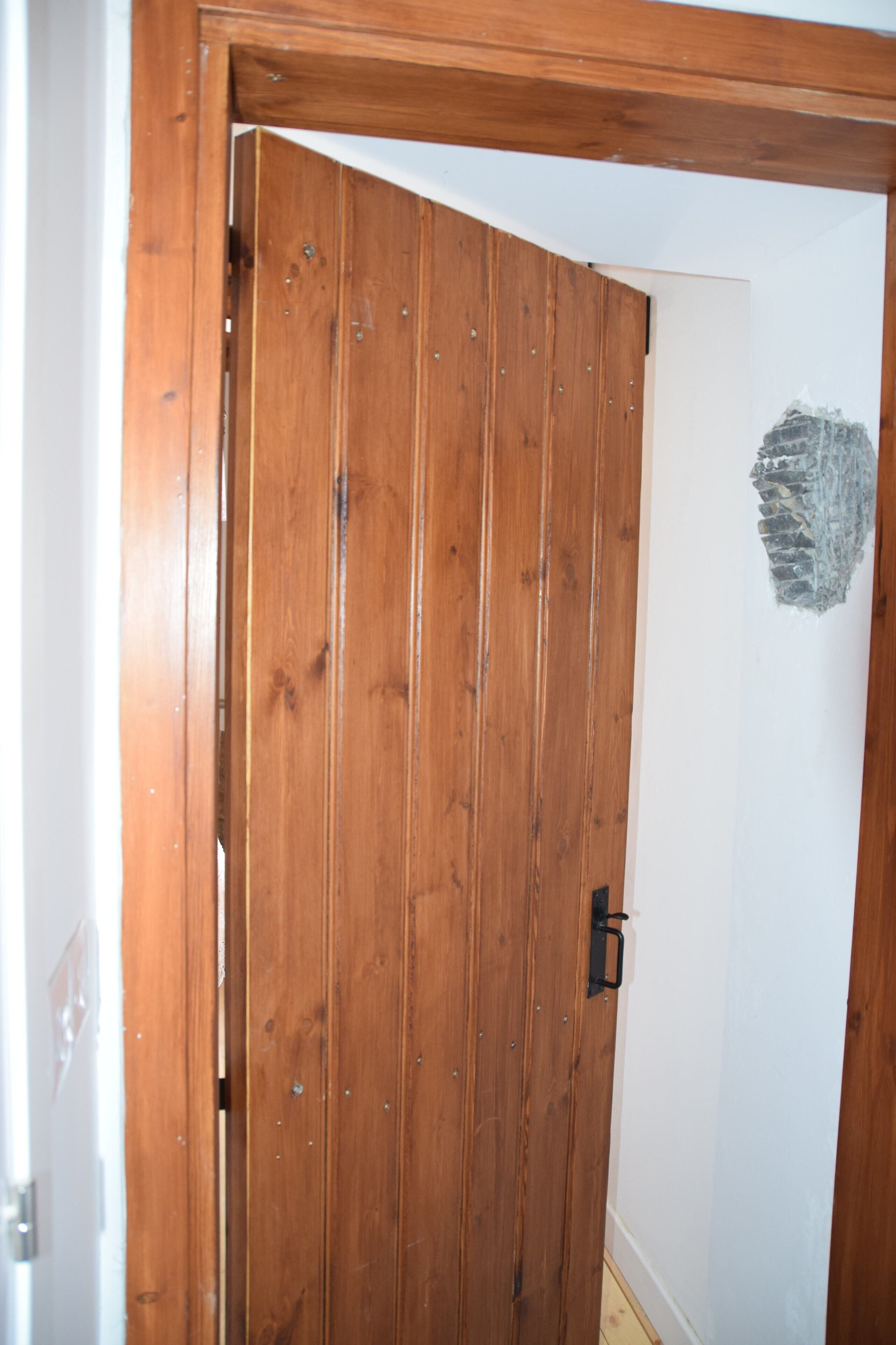 A wooden door with a black handle, a white wall with a stone-like texture, and a wooden floor.