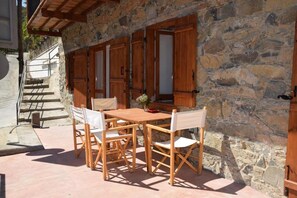 Un bâtiment en pierre avec une table et des chaises en bois à l’extérieur, un escalier et une porte dotée de volets en bois.