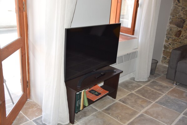 Un salon avec un téléviseur à écran plat posé sur un meuble en bois, un mur en pierre et un canapé gris.