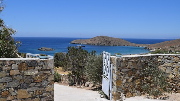 Eine Steinmauer mit einem Tor, das zu einer Küstenlandschaft führt, mit freiem Blick auf das Meer und einer kleinen Insel.
