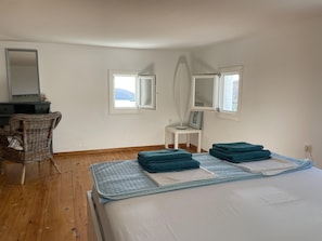 A bedroom with a bed, a chair, a desk, and two windows. - Netflix Calls it a 'paradise' (Syros)