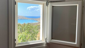 Ein Zimmer mit Fenster und Blick auf eine Küstenlandschaft, inklusive eines Gewässers und Hügeln.
