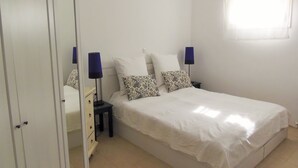 Ein Schlafzimmer mit einem Bett, zwei Nachttischen, einem Kleiderschrank und einem Fenster mit Vorhängen.