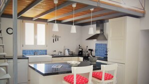 A kitchen with a central island, white bar stools with red polka dot cushions, a coffee machine, and a stove. - 'paradise' by Cnn - Delfini Bay - 3bed House (Syros)