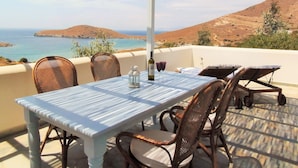 A terrace with a table and chairs overlooking a coastal landscape. - 'paradise' by Cnn - Delfini Bay - 3bed House (Syros)