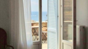 A bedroom with a bed, a chair, and a view of the sea through an open door. - 'paradise' by Cnn - Delfini Bay - 3bed House (Syros)