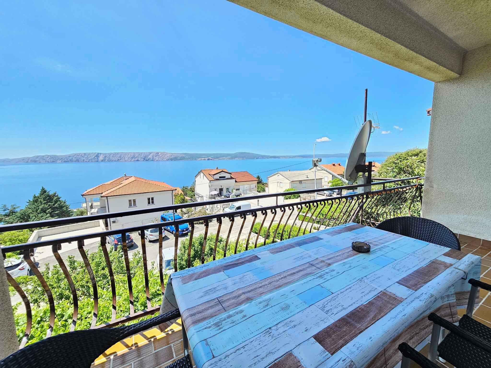 Ein Balkon mit Tisch und Stühlen mit Blick auf eine Küstenstadt und das Meer.