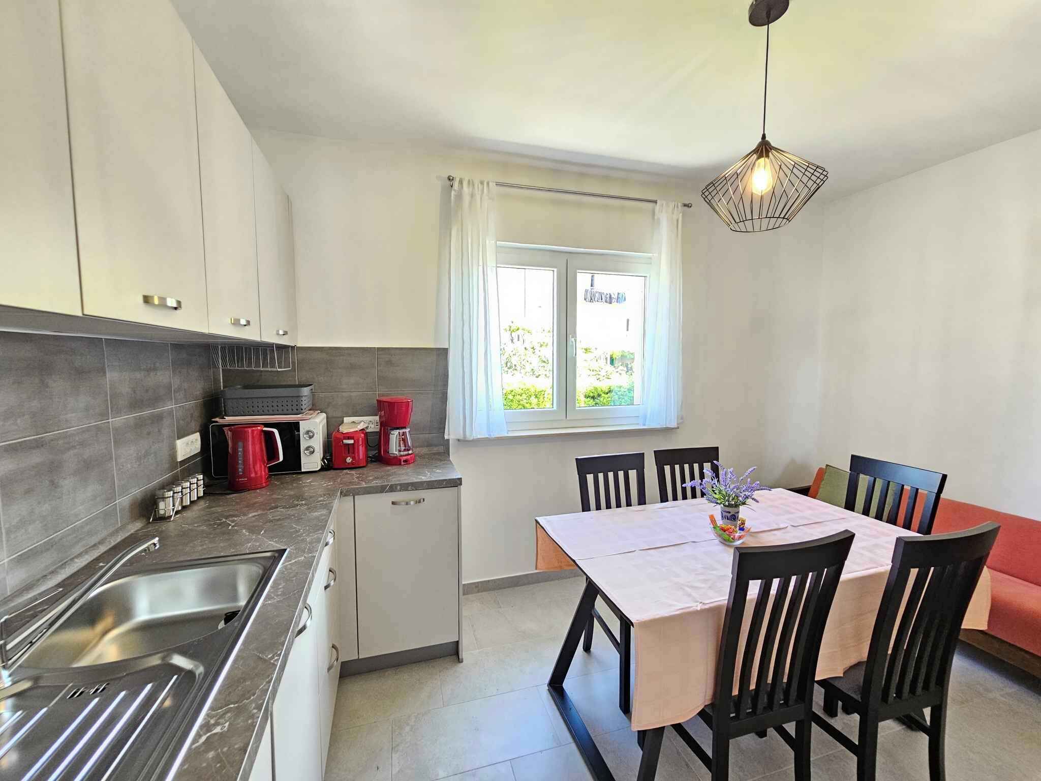 Une cuisine moderne équipée d’un évier, d’une cuisinière et d’une machine à café. On y trouve une table à manger avec des chaises, ainsi qu’une fenêtre avec des rideaux.