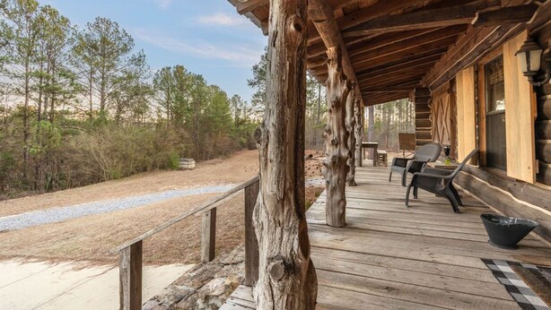 Une terrasse en bois agrémentée de piliers rustiques, d’un espace salon extérieur et offrant une vue sur la forêt environnante.
