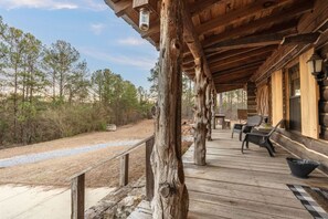 A wooden deck with rustic pillars, outdoor seating, and a view of the surrounding forest. - A True Logger's Cabin in Prattville (Prattville)