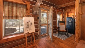 L’intérieur d’un chalet en rondins, avec une tête de cerf accrochée au mur, un tableau posé sur un chevalet et une porte portant l’inscription « Scout ».