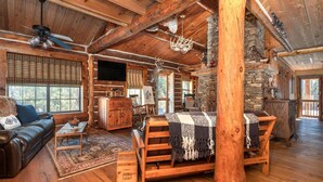 L’intérieur d’un chalet rustique, avec un canapé en bois, une cheminée en pierre et une grande structure en poutres apparentes.