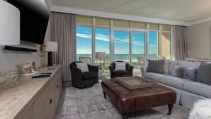 Ein modernes Hotelzimmer mit großem Fenster, einer Couch, einem Sessel, einem Couchtisch und einem Fernseher.