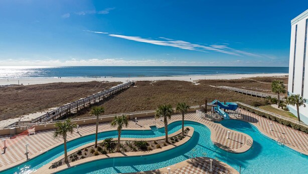 Poolbereich mit Rutsche, Palmen und Blick auf den Strand.